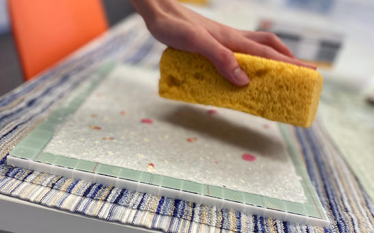 Hand holding a sponge over hand made paper