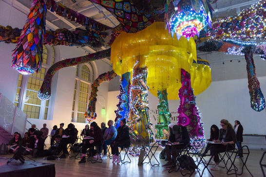 Visitors sketching in low light under the large sculpture by Joana Vasconcelos