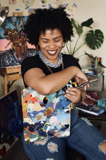 Color photograph of Zahirah Nur Truth seated, holding a painting.