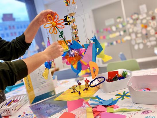 A visitor adds brightly colored paper and materials to a hanging mobile