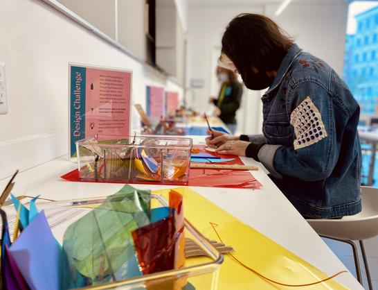 A visitor sits at a desk with lots of brightly colored materials completing an artmaking activity