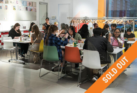 A lively group of people are seated around tables engaging in arts and crafts. The room is bright and modern, and the atmosphere is creative and cheerful. Various crafting materials are scattered on the tables. The image has a "Sold Out" banner diagonally across it.