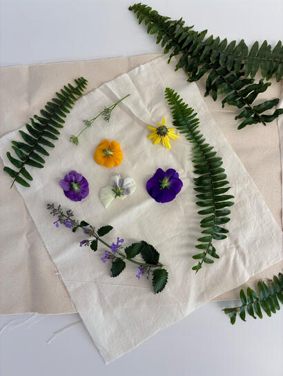 Assorted flowers and fern leaves arranged on a white cloth over beige fabric on a white surface.