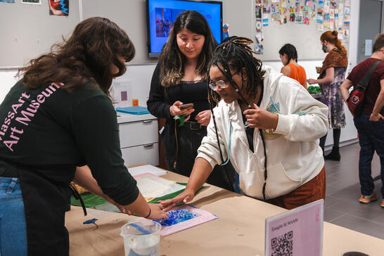 Several people work together on an arts and crafts project at a table in a brightly lit art museum space.