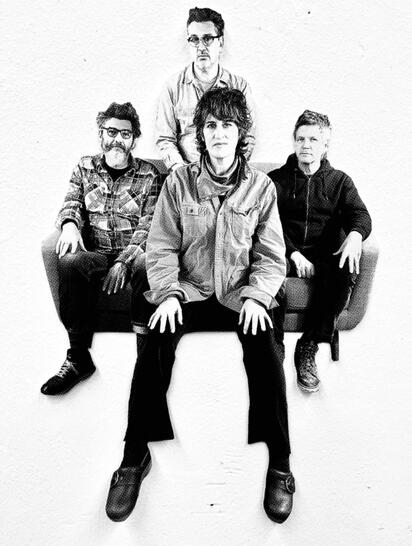 Four band members posing together on a couch.