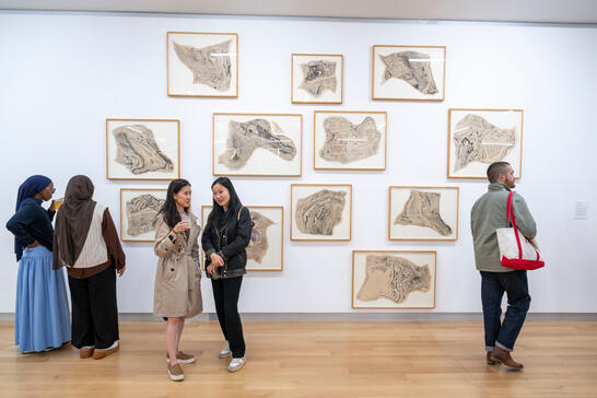 People viewing a gallery wall covered in framed abstract art prints.