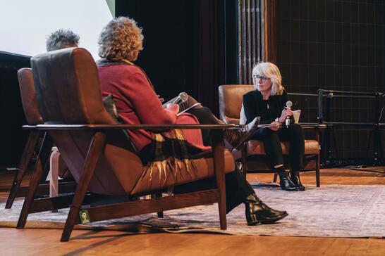 Three people seated in chairs on a stage having a discussion with microphones.