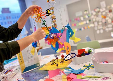 A visitor adds brightly colored paper and materials to a hanging mobile