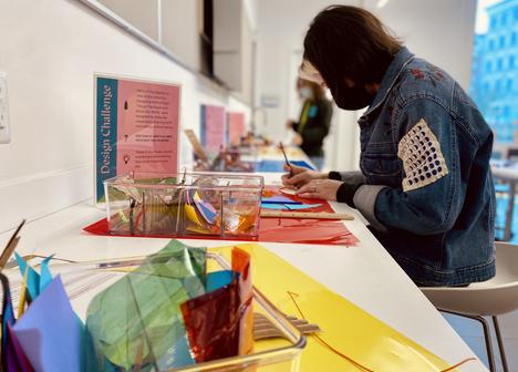A visitor sits at a desk with lots of brightly colored materials completing an artmaking activity