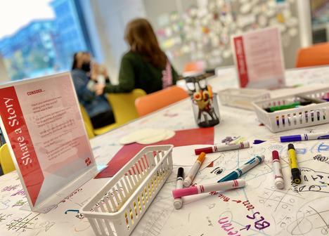 A table with markers and paper with two people in the background