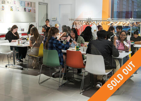 A lively group of people are seated around tables engaging in arts and crafts. The room is bright and modern, and the atmosphere is creative and cheerful. Various crafting materials are scattered on the tables. The image has a "Sold Out" banner diagonally across it.