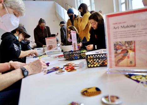 People of various ages sitting around a table, engaged in arts and crafts activities in a bright room.
