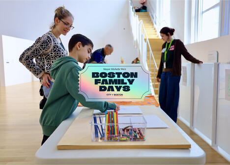 A boy drawing with crayons at a Boston Family Days event, with adults nearby in a bright art space.