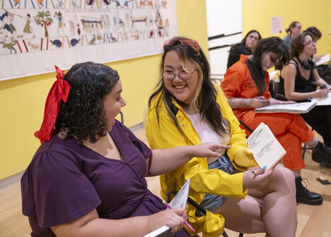 Two people smiling and sharing sketches in an art class, with others drawing in the background.