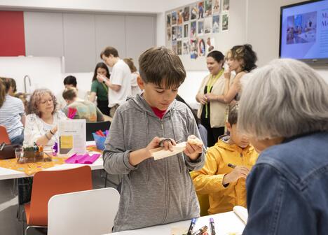 A young boy in a grey hoodie cuts a piece of paper during an art workshop.