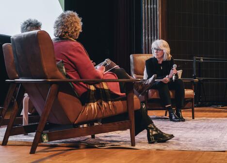 Three people seated in chairs on a stage having a discussion with microphones.