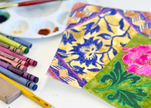 Image of crayons, pencil, eraser, and brightly colored patterns on paper made using ink resist technique