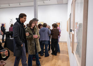 A lively art gallery scene with people admiring framed artworks on white walls. Visitors, casually dressed, hold drinks, showing engagement and interest.