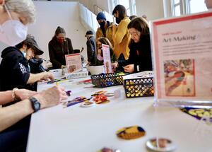 People of various ages sitting around a table, engaged in arts and crafts activities in a bright room.