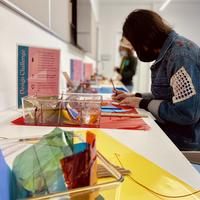 A visitor sits at a desk with lots of brightly colored materials completing an artmaking activity