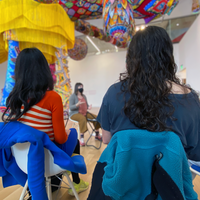 Visitors sit in a circle under a colorful sculpture and installation.