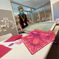 An artist holds a silkscreen with brightly colored and decorated bandanas in on a table
