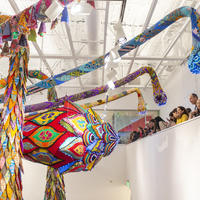 Viewers stand on a balcony in the museum looking out at the brightly colored huge sculpture hanging from the ceiling