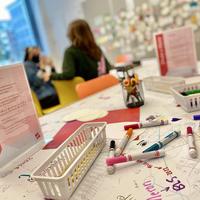 A table with markers and paper with two people in the background