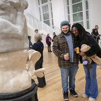 An image of two people holding drinks looking at a sculpture in the Paine Gallery