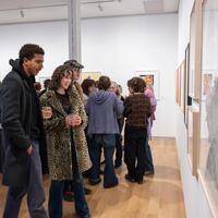 A lively art gallery scene with people admiring framed artworks on white walls. Visitors, casually dressed, hold drinks, showing engagement and interest.