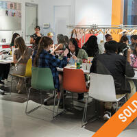 A lively group of people are seated around tables engaging in arts and crafts. The room is bright and modern, and the atmosphere is creative and cheerful. Various crafting materials are scattered on the tables. The image has a "Sold Out" banner diagonally across it.