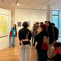 A group of people listens to a guide in front of colorful artworks in a modern gallery. The atmosphere is attentive and curious.
