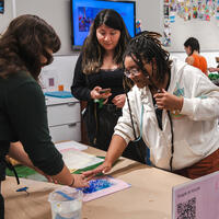 Several people work together on an arts and crafts project at a table in a brightly lit art museum space.