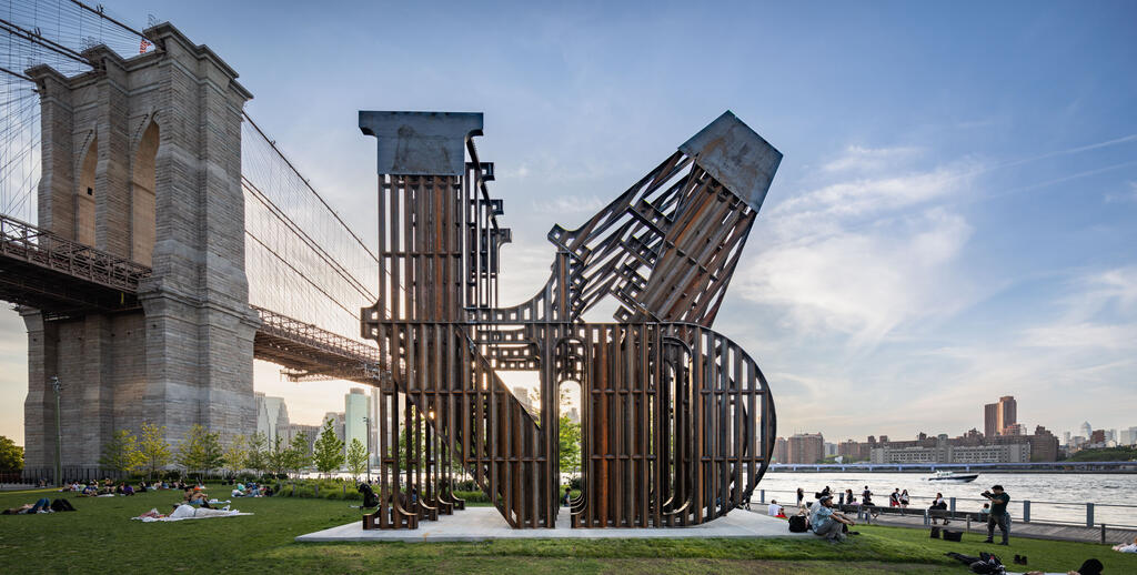 Large steel sculpture with the letters LAND sited in front of the Brooklyn Bridge at dusk