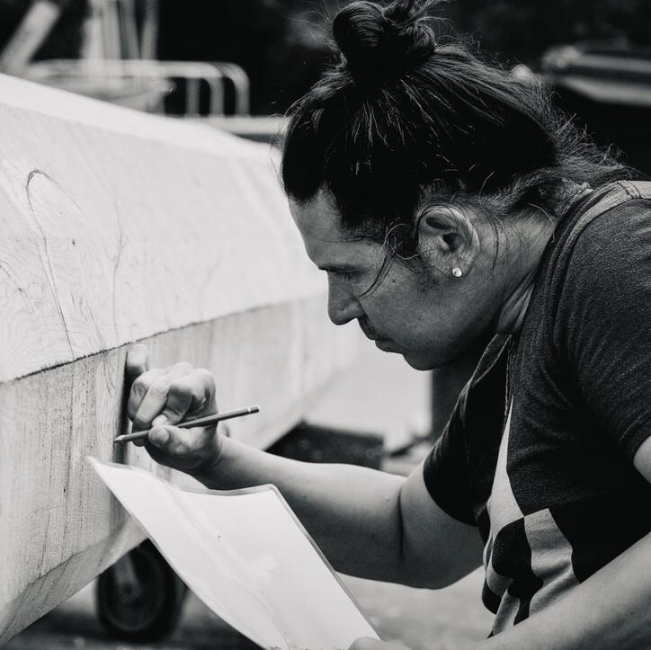 black and white portrait of the artist Nicholas Galanin shown in profile with his hair in a top knot, drawing and holding a piece of paper