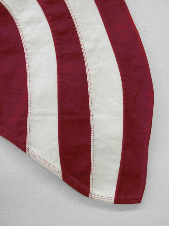 Close-up of a red and white striped fabric, likely part of a flag, against a plain light gray background.