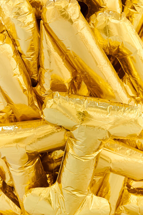 A pile of shiny gold foil balloons shaped like the letter T overlapping each other.