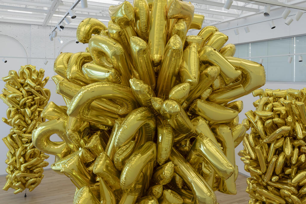 Clusters of shiny gold balloons shaped like letters fill a bright, modern gallery space.