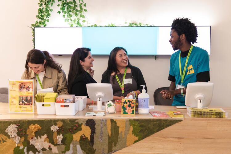 Four people smiling and laughing with one another behind a check-in desk.