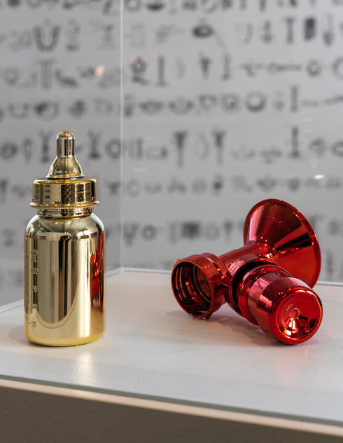 Gold chromed baby bottle and shiny red breast pump flange.
