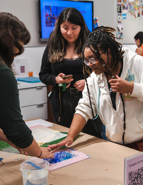Several people work together on an arts and crafts project at a table in a brightly lit art museum space.