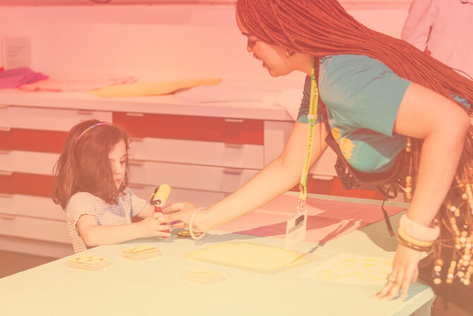 MAAM Museum Attendant / student educator handing a printmaking roller to a young child artist.